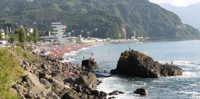 Sarpi Beach Batumi rocky shoreline with crowded beach, colorful umbrellas, green hills, and Black Sea, Georgia