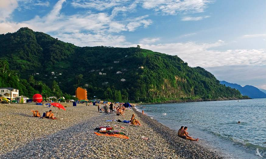 Kvariati Beach Batumi pebble shore with sunbathers, green forested hills, and calm Black Sea waters, Georgia