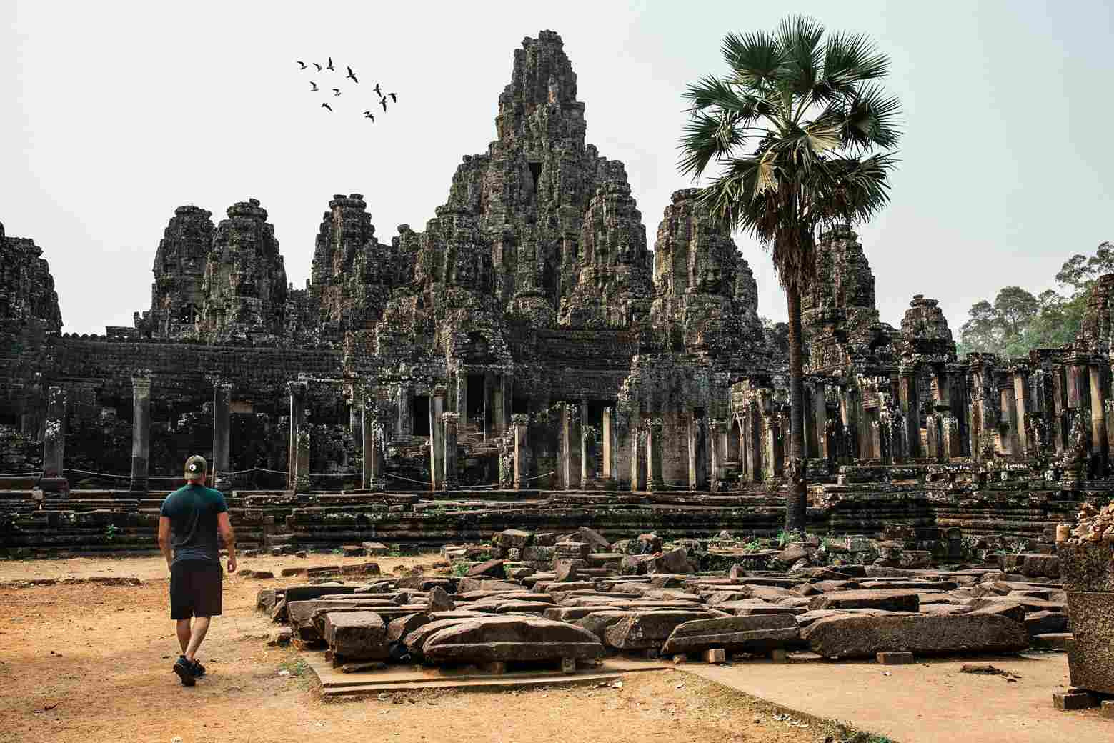 Tourist walking toward ancient Bayon Temple ruins Angkor Wat Siem Reap Cambodia