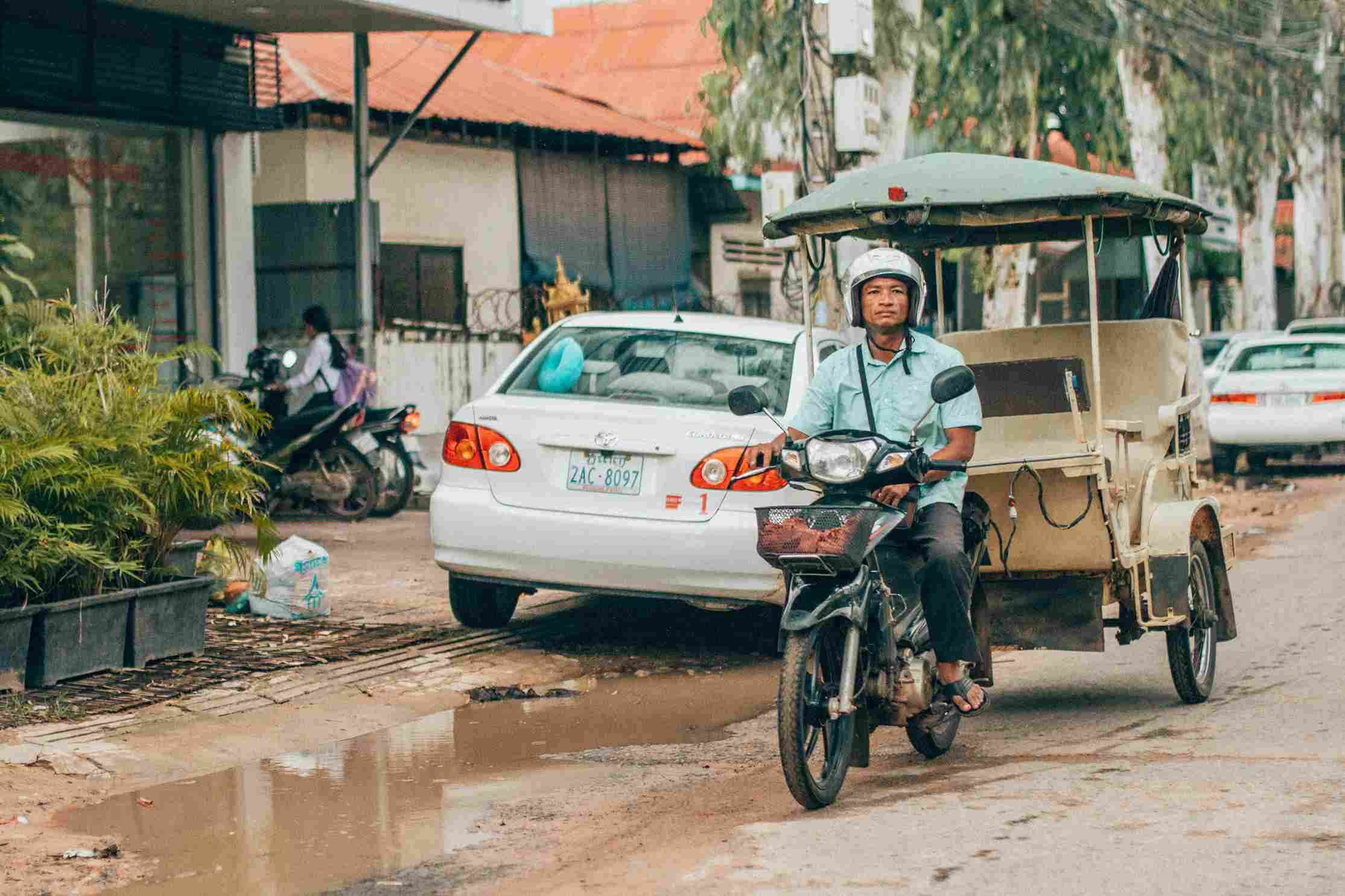 Tuk tuk driver riding motorcycle rickshaw on busy Phnom Penh Cambodia street